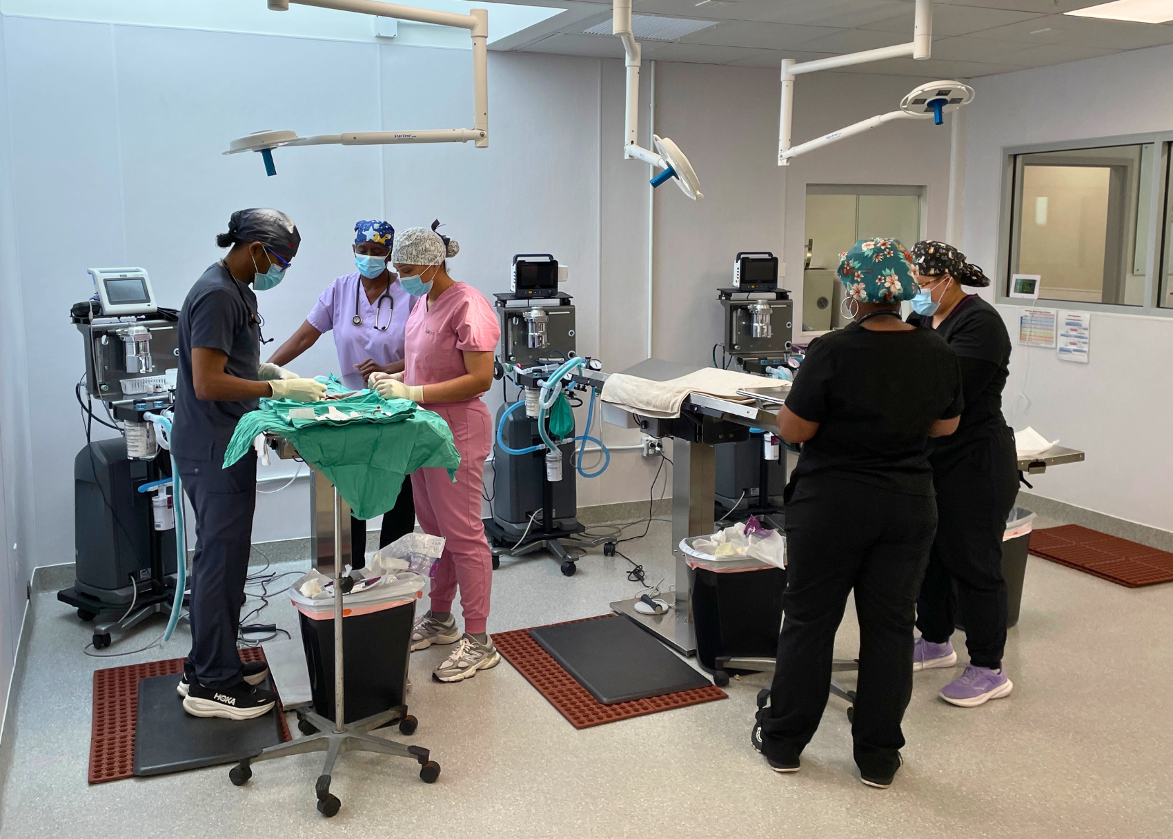 Veterinary clinic staff standing in operating room around two tables prepping for surgery with no animals present