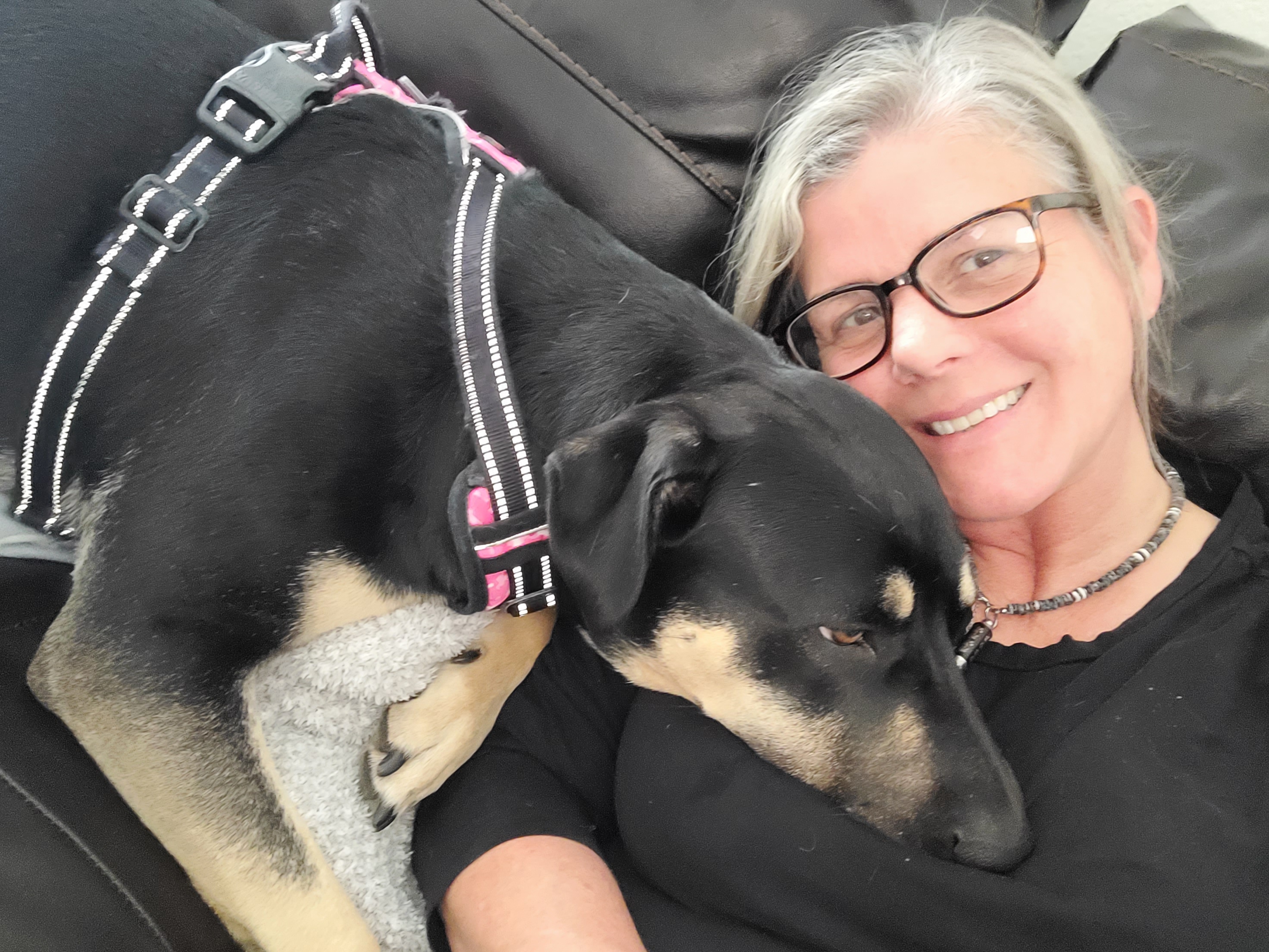 Kona, a large black and tan dog, sleeping on her adoptive mom, who is smiling at the camera.