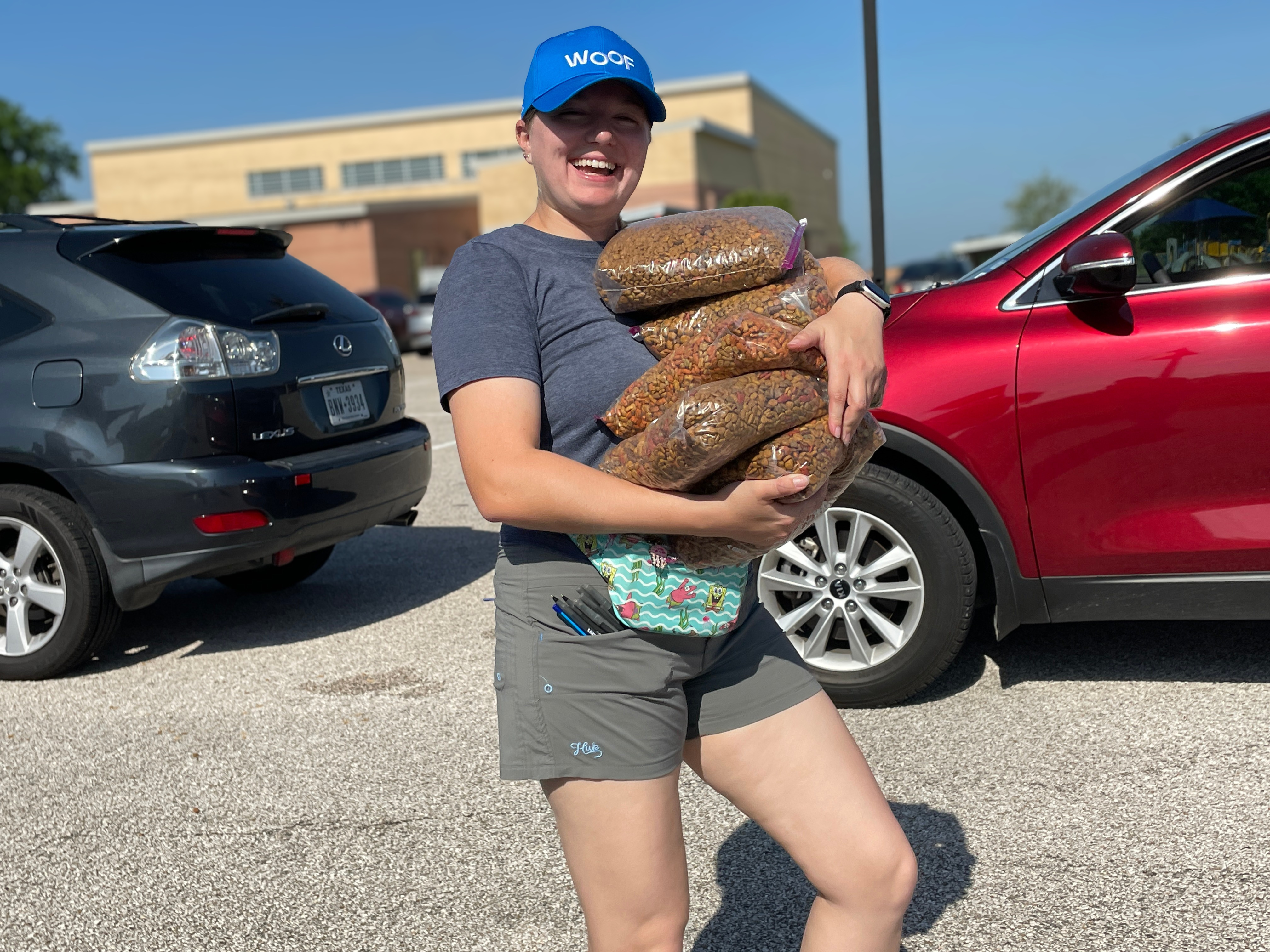 Woman outdoors, smiling at the camera, holding four bags of dog food