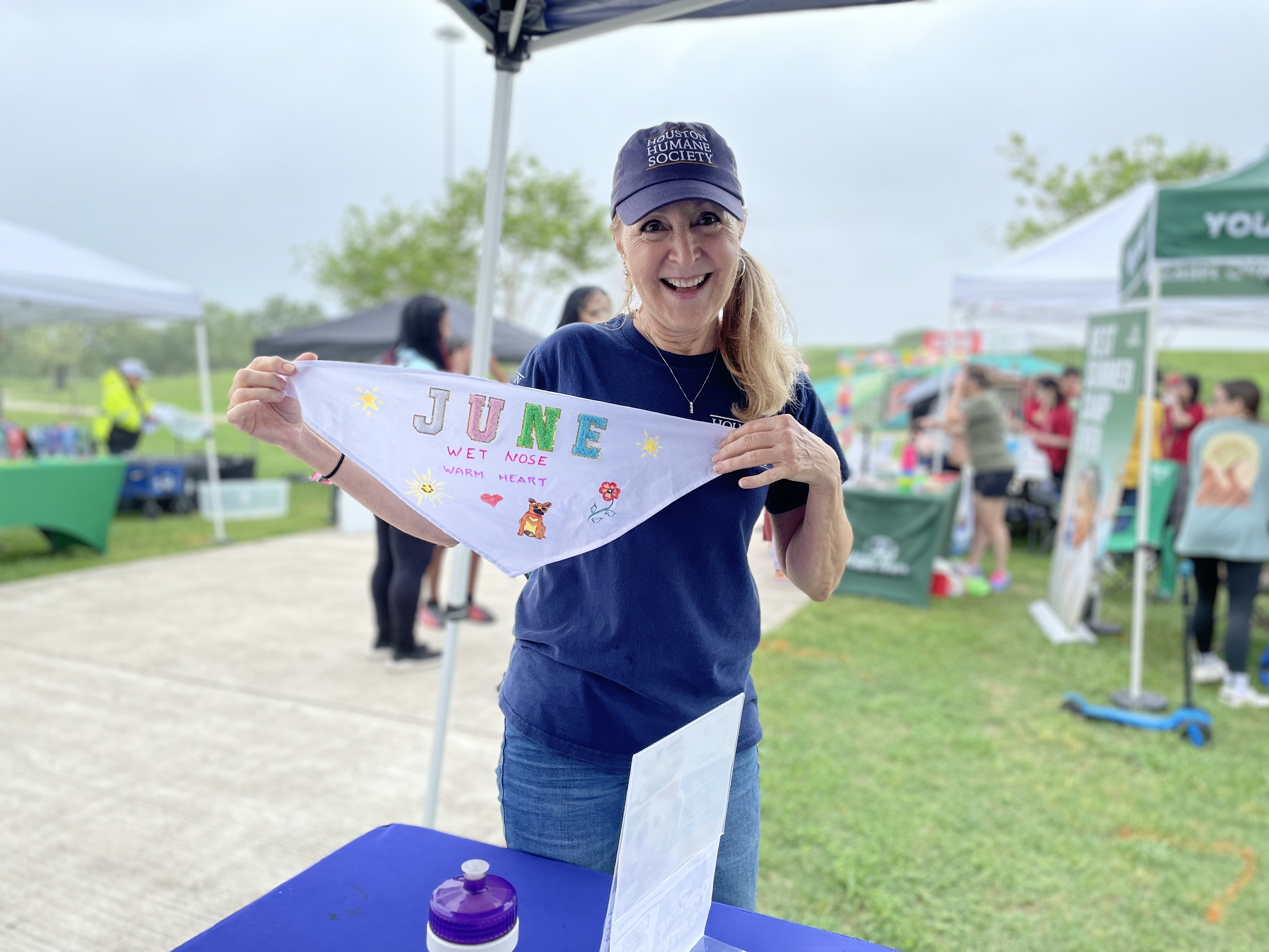 Brigitte, a volunteer, standing outdoors, holding a handmade bandana that reads "June".