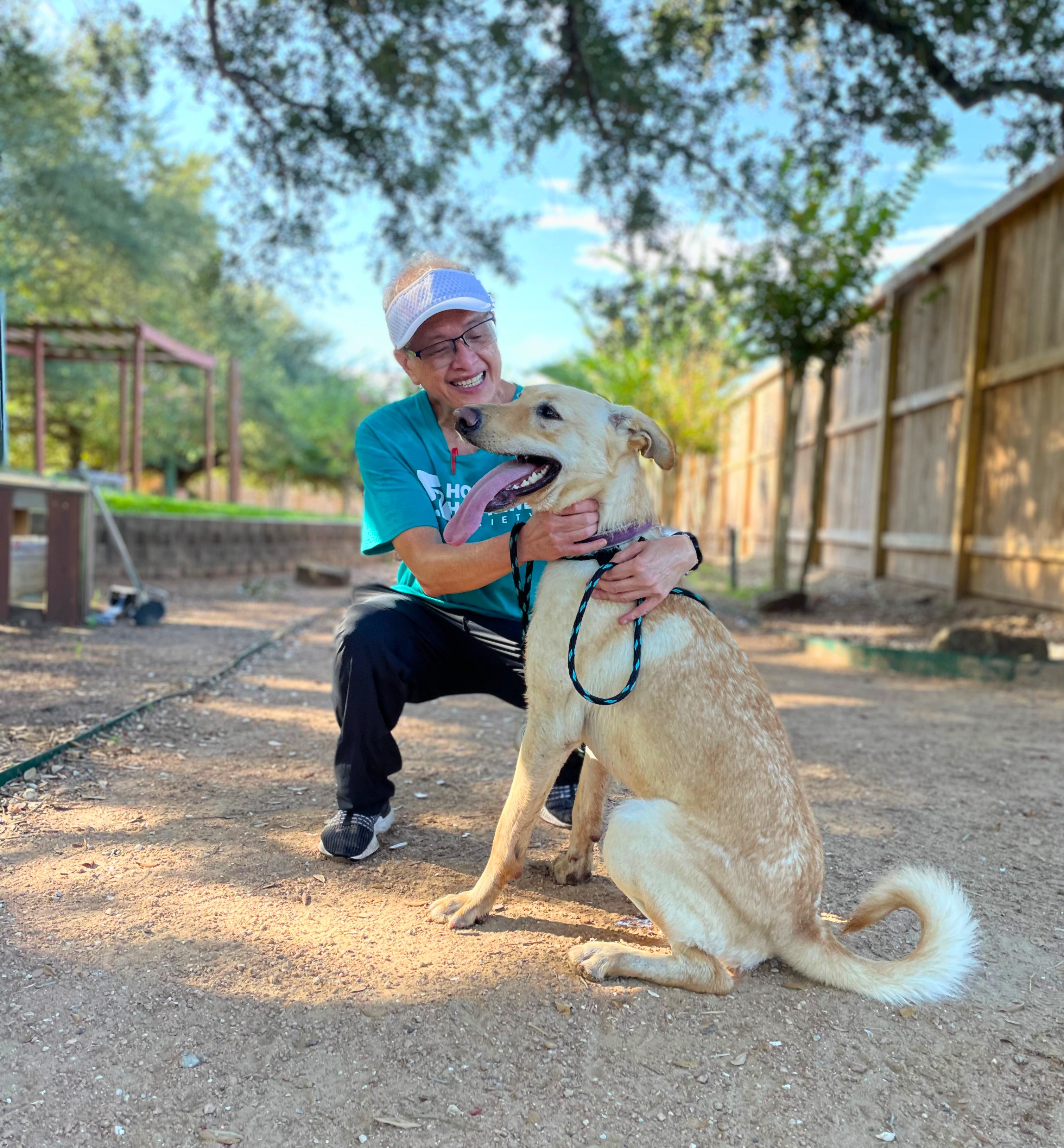 Gene, a Houston Humane Society volunteer, kneeling next to a shelter dog outdoors.