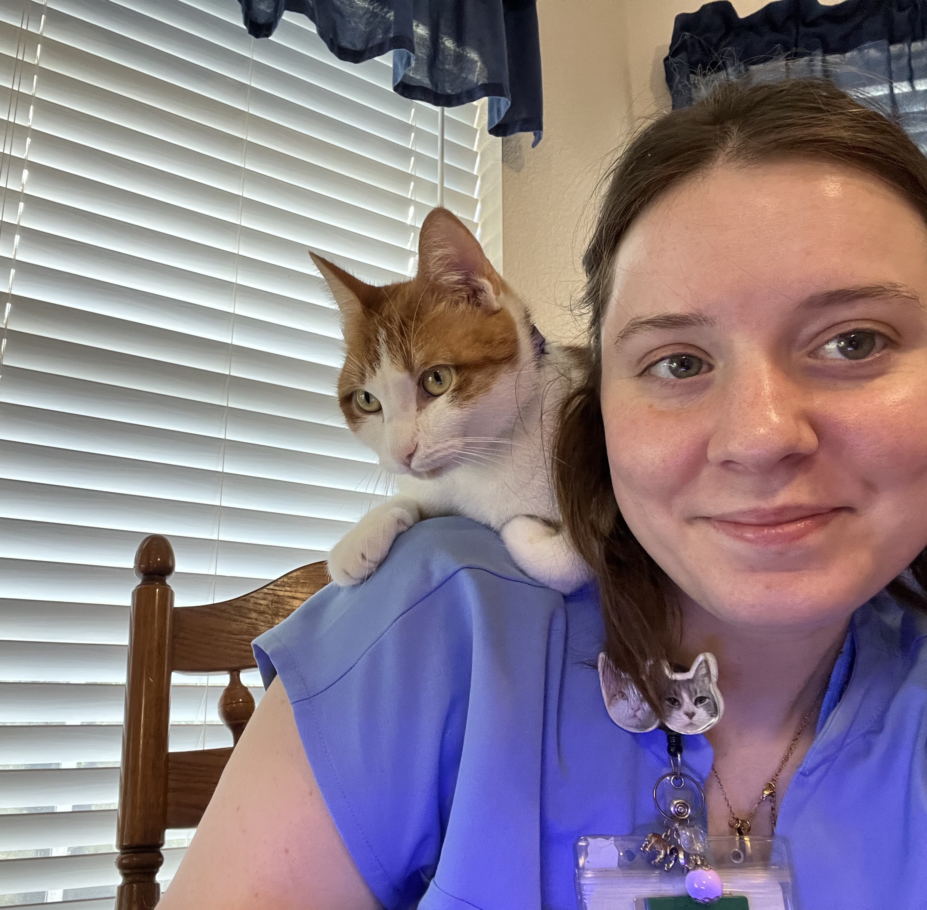 Close up of a woman sitting in a chair. There is an orange and white cat perched on her shoulder.