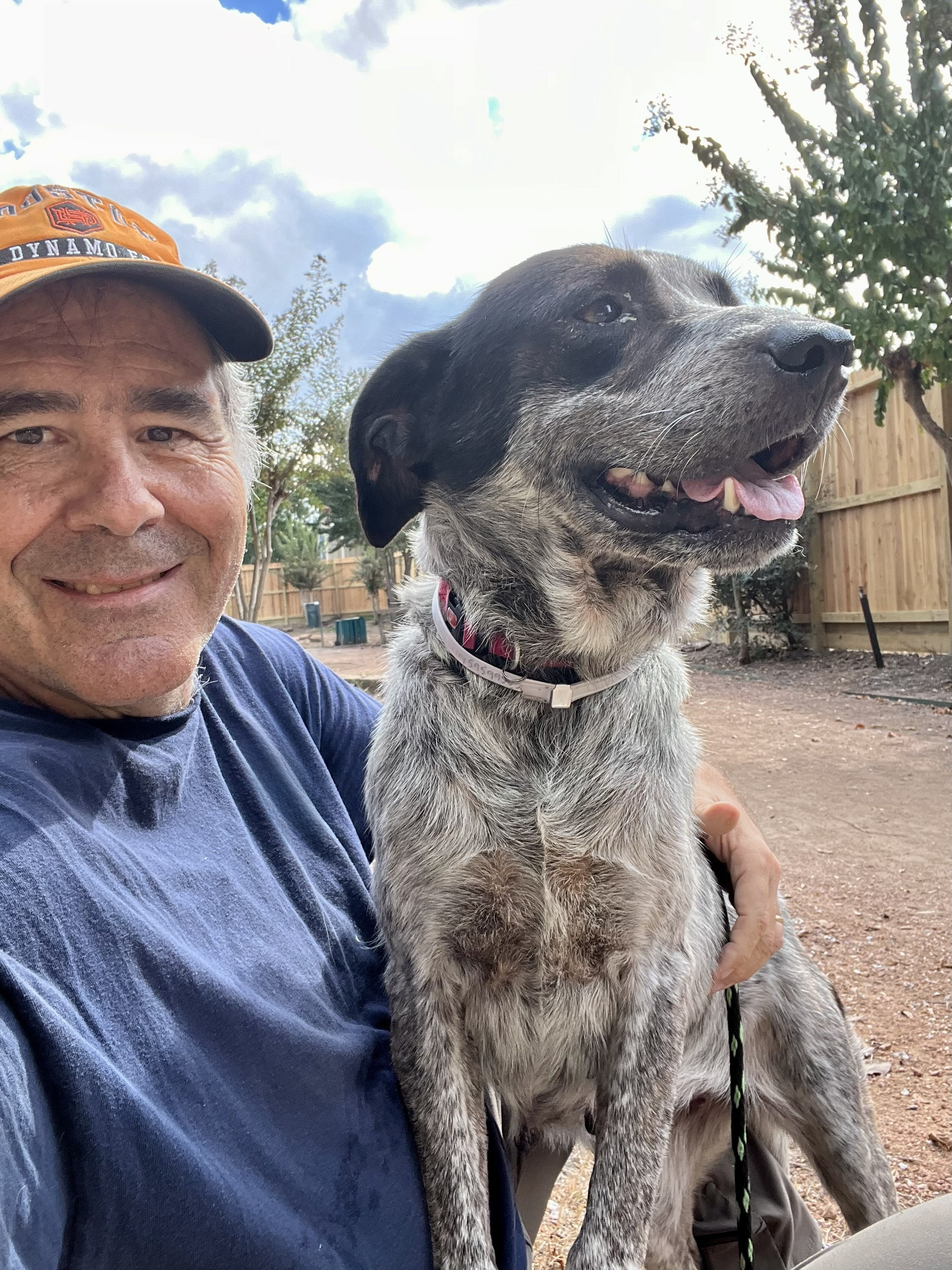 Selfie of a man outdoors with an adult dog in his lap. The man is smiling at the camera.